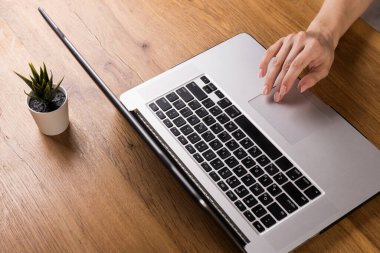 Eski ahşap masada dizüstü bilgisayarla çalışan bir kadın. Ahşap masa arkasında ofis malzemeleri ve aletlerin karışımı. Boşluğu kopyala.