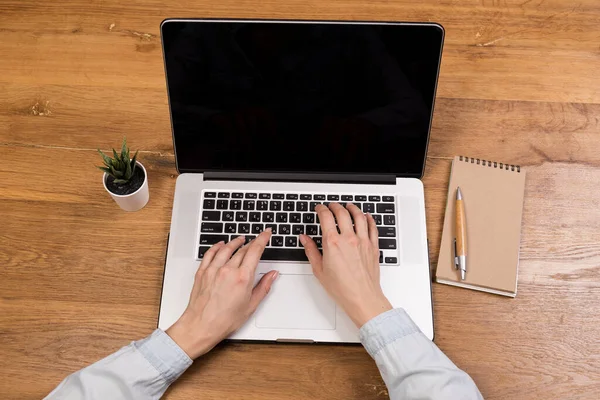 Eski ahşap masada dizüstü bilgisayarla çalışan bir kadın. Ahşap masa arkasında ofis malzemeleri ve aletlerin karışımı. Boşluğu kopyala.