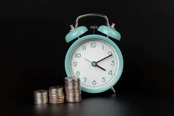 ビジネス隠喩の概念の時間はお金の概念である 黒い背景の青い目覚まし時計とコイン ストック写真