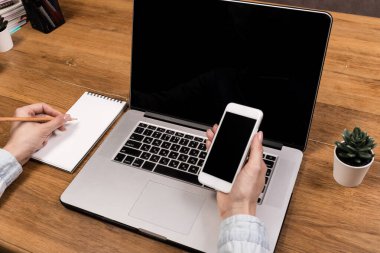 Bilgisayardaki işlemi onaylayan bir mesaj almak için elinde akıllı telefon tutan bir kadının kesilmiş görüntüsü. Bir kadın, verileri bluetooth üzerinden netbook ile senkronize etmek için mobil bir uygulama kullanıyor.