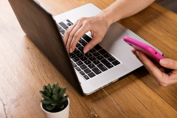 Bilgisayardaki işlemi onaylayan bir mesaj almak için elinde akıllı telefon tutan bir kadının kesilmiş görüntüsü. Bir kadın, verileri bluetooth üzerinden netbook ile senkronize etmek için mobil bir uygulama kullanıyor.