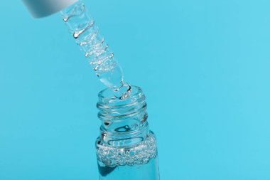 Mavi arka planda pipetli kozmetik ya da tıbbi cam şişe, yakın planda. Cilt bakımı kavramı. 