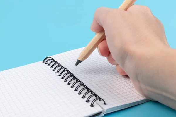 Hand with pencil writing in the notebook isolated over blue background