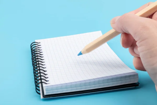 Mão Com Lápis Escrevendo Caderno Isolado Sobre Fundo Azul — Fotografia de Stock