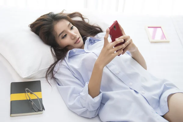 Güzel kadın telefon yatakta mutlu sabah oynarken.