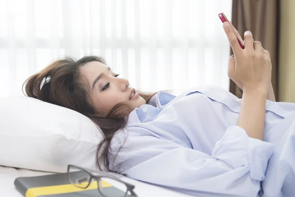 Güzel kadın telefon yatakta mutlu sabah oynarken.