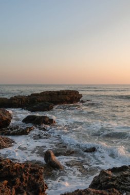 Güneşli bir günde Portekiz 'de Atlantik Okyanusu' ndaki kayalara bakarak gün batımı