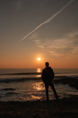 Güneşli bir günde Portekiz 'de Atlantik Okyanusu' nda gün batımına bakan bir adam.