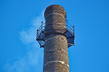 Fabrika bacası mavi gökyüzüne karşı tütüyor