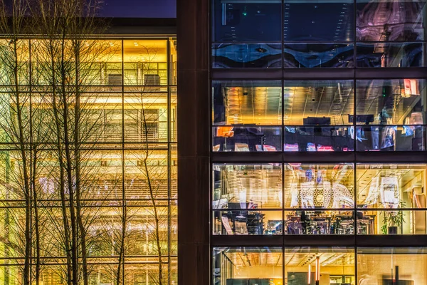 Contemporary office with a glazed facade illuminated at night with visible interiors in the financial district. Modern building or headquarter where people invest or trade in the banking industry. Here high business and tech jobs take place