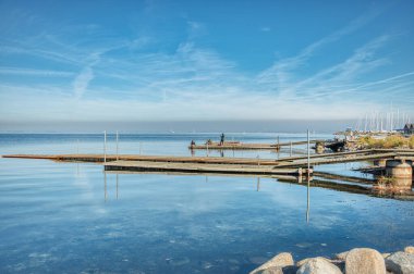İnsanlar, güneş ısındıkça ahşap bir iskelede dinleniyor, su kristal gibi berrak, tatil molası, dinlenme ve tatil konseptini iletiyor. Huzurlu insanlar sakin bir Baltık Denizi kıyısında bir iskelede uzanmış fotoğraf çekiyorlar.
