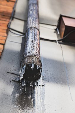 Dondurucu koşullardan dolayı buz saçakları olan paslı bir drenaj borusundan süzülen su. Endüstriyel, çevresel ve iklim değişikliği kavramını sürdürmeyen su birikintisi veya oluklar taşır