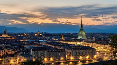 Gün batımında Giusto Gervasutti 'nin balkonundan yükselen Torino silueti zarif şehir bloklarının üzerinden yükseliyor. Sıcak ışıklar Alpler 'in silueti dramatik bir gökyüzünün altında parlarken