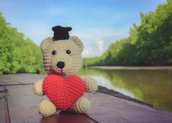 Ours en peluche avec cœur rouge assis sur un pont en bois près de la rive - ton vintage — Photo