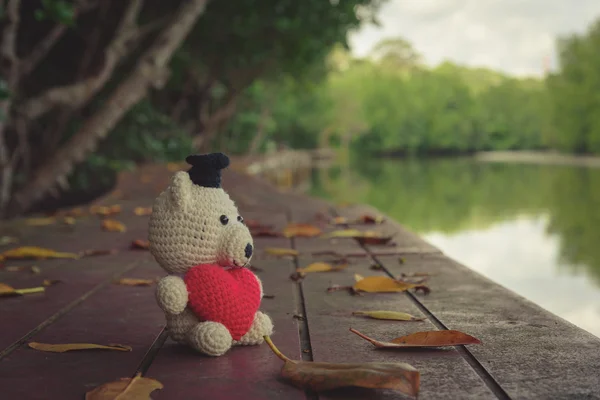 Ours en peluche avec cœur rouge assis sur un pont en bois près de la rive - ton vintage — Photo