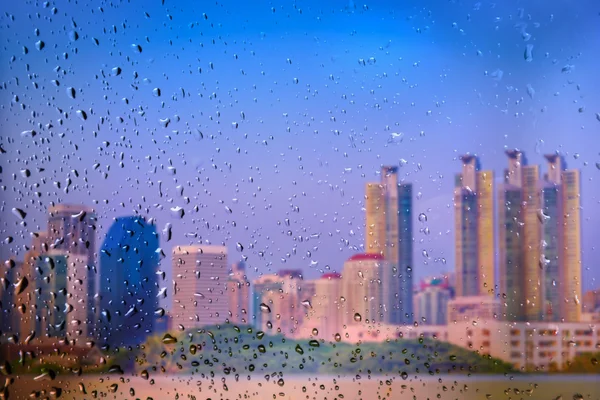 Gota de lluvia en una ventana de cristal con fondo borroso de la ciudad. Enfoque selectivo — Foto de Stock