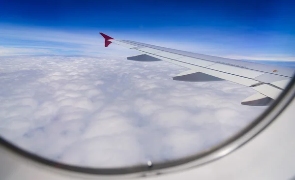 Ala de avión volando por encima de las nubes en el fondo del cielo azul a través de la ventana . —  Fotos de Stock