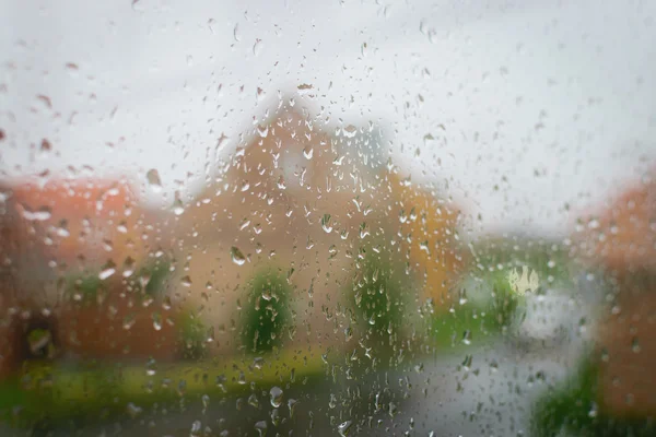 Gotas de lluvia en el cristal de una ventana, casa de desenfoque en el fondo . — Foto de Stock