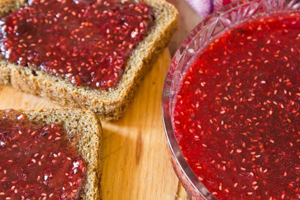 Raspberry jam and a slice of black bread — Stock Photo, Image