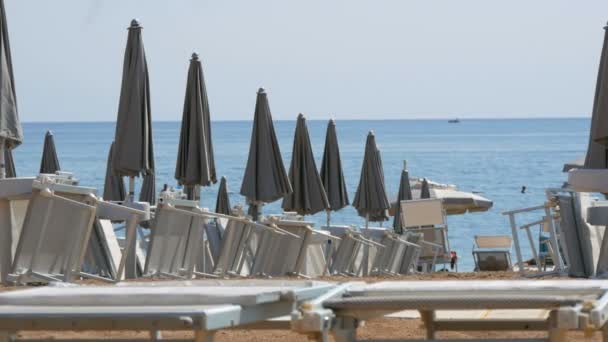 Tomma stranden på kusten av en badort, ensamma solstolar och nära grå strand parasoller, slet bort badorten på grund av covid 2019, coronavirus, karantän, Adriatiska havet, Montenegro — Stockvideo