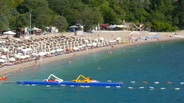 Becici, Montenegro - August 26, 2020: Beach with a lot of umbrellas and sun loungers on the Adriatic coast, people sunbathe and swim in the sea on vacation — Stock Video