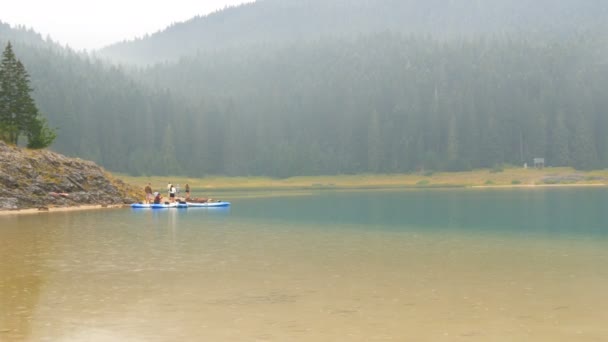 Zwarte meer in Montenegro tijdens de regen. Regendruppels vallen op het wateroppervlak. De betoverende schoonheid van de ongerepte natuur van het meer, de bergen en het bos. Groep toeristen op sabords of kajaks — Stockvideo