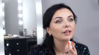 Genç, güzel, gösterişli kadın aynanın önünde yüz makyajı ve ruj sürüyor.