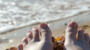 Dişi ayakları, deniz kabuğu sahilinde ayak parmakları, deniz ve dalgalar. Rahatlama konsepti, yaz tatili. POV