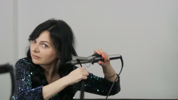 Kamenskoe, Ukraine - October 12, 2020: A beautiful spectacular young woman winds her long black hair on a special iron to create curls close up view — Stock Video