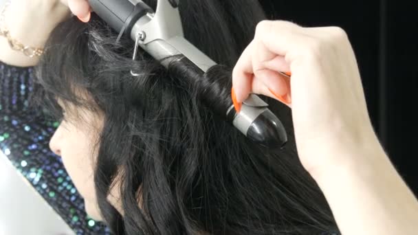 Seorang wanita muda yang spektakuler angin rambut hitam panjang pada besi khusus untuk menciptakan ikal menutup pandangan — Stok Video