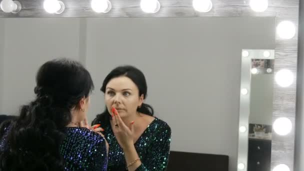 Jovem bela mulher vistosa na frente de um espelho aplica maquiagem e fundação ou corretor com as mãos — Vídeo de Stock