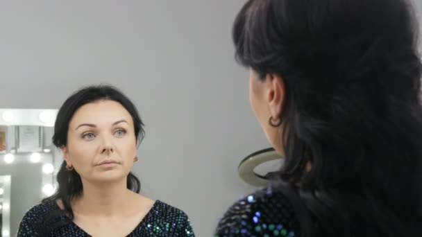 Mladá krásná showy žena v přední části zrcadla aplikuje tvář a oční make-up se speciálním štětcem