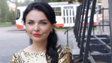 Göz kamaştırıcı bir akşam makyajıyla ışıl ışıl parlayan altın rengi elbisesiyle sokakta tramvaylar geçiyor, yayalar geçiyor.