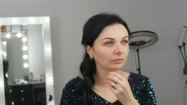 Jonge mooie opzichtige vrouw in de voorkant van een spiegel brengt make-up en stichting of concealer met haar handen — Stockvideo