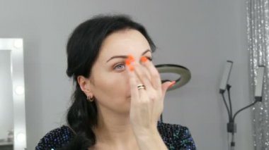 Aynanın önünde duran güzel ve gösterişli genç kadın elleriyle makyaj ve fondöten ya da kapatıcı sürüyor.