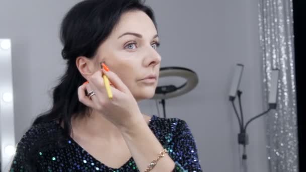 Jonge mooie opzichtige vrouw in de voorkant van een spiegel brengt make-up en stichting of concealer met een speciale borstel — Stockvideo