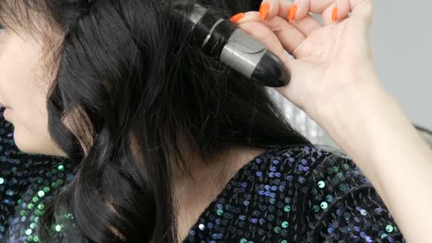 Красивая эффектная молодая женщина ветра ее длинные черные волосы на специальном утюге, чтобы создать кудри вблизи зрения — стоковое видео