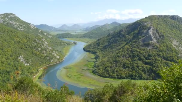 Río azul que fluye a través del valle verde hacia montañas distantes. Curvas y curvas del río Crnojevica en el parque nacional de Montenegro, serpenteando a través del pantano entre colinas en camino al lago Skadar — Vídeos de Stock