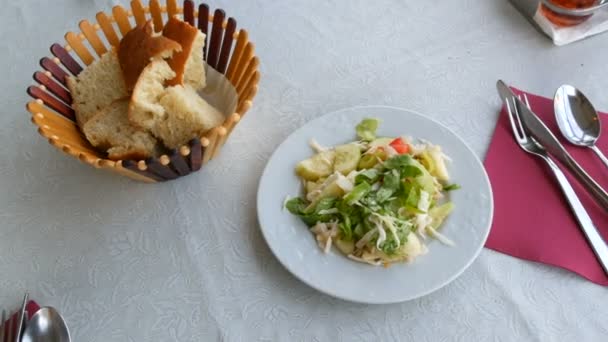 Nakrycie do stołu w restauracji. Chleb w koszyku, sałatka warzywna w talerzu, nóż sztućcowy, widelec, łyżka na czerwonej serwetce — Wideo stockowe