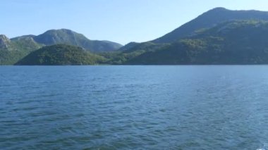 Mavi nehir yeşil vadiden uzak dağlara doğru akıyor. Karadağ milli parkındaki Crnojevica nehrinin kıvrımları ve kıvrımları, Skadar Gölü 'ne giden tepelerin arasında bataklıktan geçiyor.