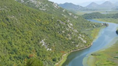 Mavi nehir yeşil vadiden uzak dağlara doğru akıyor. Karadağ milli parkındaki Crnojevica nehrinin kıvrımları ve kıvrımları, Skadar Gölü 'ne giden tepelerin arasında bataklıktan geçiyor.