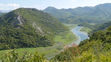 Mavi nehir yeşil vadiden uzak dağlara doğru akıyor. Karadağ milli parkındaki Crnojevica nehrinin kıvrımları ve kıvrımları, Skadar Gölü 'ne giden tepelerin arasında bataklıktan geçiyor.