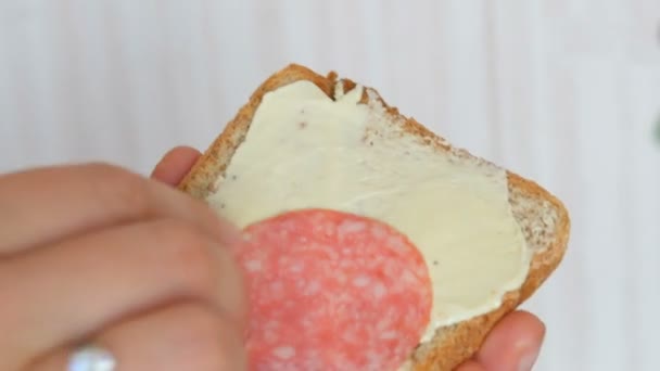 Uma mão de mulher põe pedaços finos de salsicha de salame em uma fatia de pão torrado. Café da manhã — Vídeo de Stock