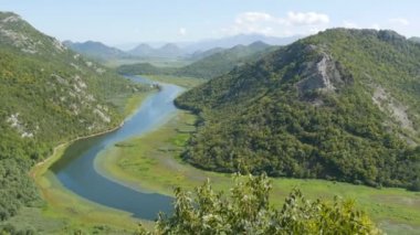 Mavi nehir yeşil vadiden uzak dağlara doğru akıyor. Karadağ milli parkındaki Crnojevica nehrinin kıvrımları ve kıvrımları, Skadar Gölü 'ne giden tepelerin arasında bataklıktan geçiyor.
