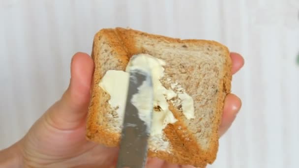 Una mano de mujer esparce mantequilla con un cuchillo de mesa sobre pan tostado tostado. Desayuno por la mañana — Vídeo de stock
