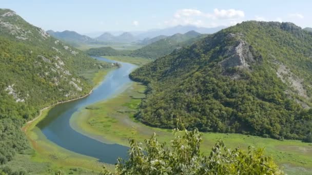 Blauwe rivier stroomt door groene vallei naar verre bergen. Bochten en bochten van de rivier Crnojevica in het nationale park van Montenegro, meanderend door het moeras tussen de heuvels op weg naar het meer Skadar — Stockvideo