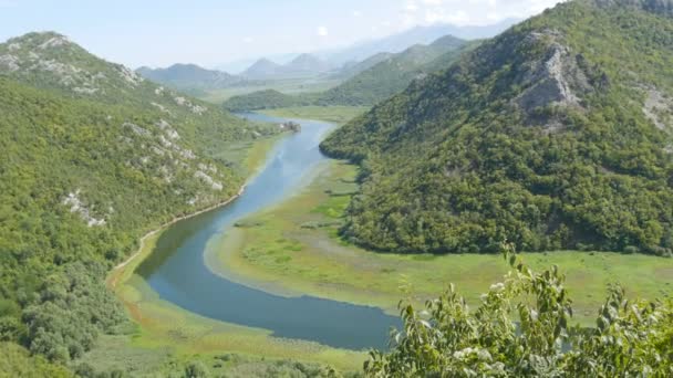 Fiume blu che scorre attraverso la valle verde verso montagne lontane. curve e curve del fiume Crnojevica nel parco nazionale del Montenegro, serpeggiando attraverso la palude tra le colline sulla strada per il lago Skadar — Video Stock