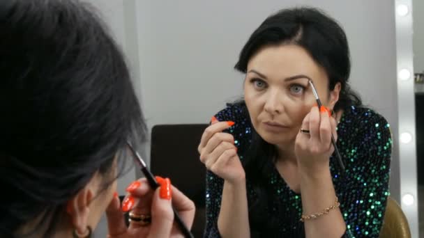 Jonge mooie opzichtige vrouw in de voorkant van de spiegel brengt gezicht en oog make-up met een speciale borstel — Stockvideo