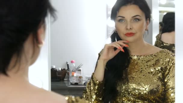 鏡の前にはスパンコールの輝くゴールドのドレスを身にまとい、彼女の姿を見ると、美しい夕暮れの若い女性が目を輝かせている。 — ストック動画