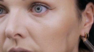 Aynanın önündeki güzel, gösterişli genç kadın özel bir fırçayla yüz ve göz makyajı yapıyor.